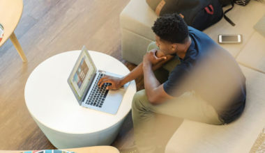 man sitting with laptop and phone looking puzzled