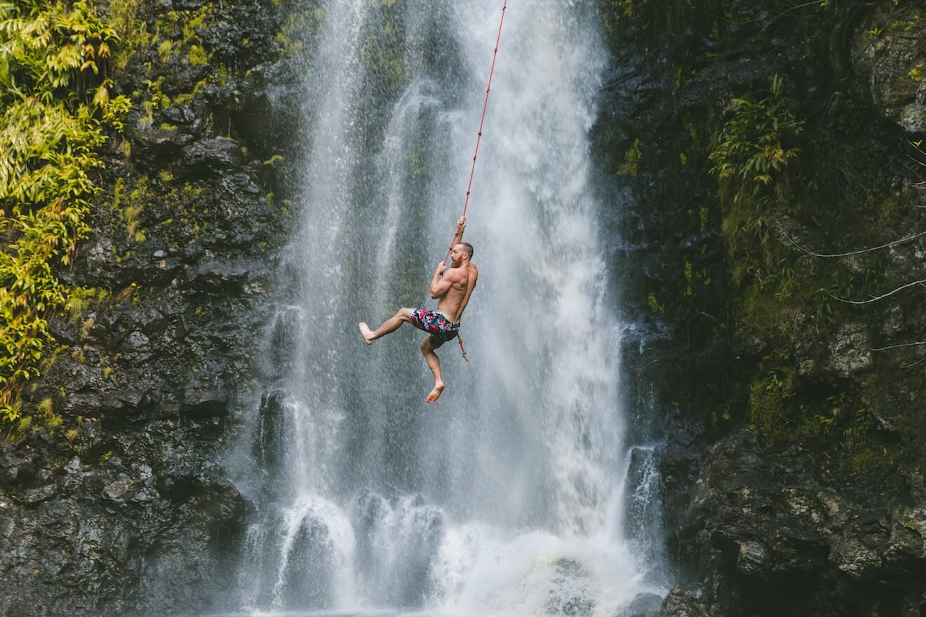 Man swinging from rope by waterfall