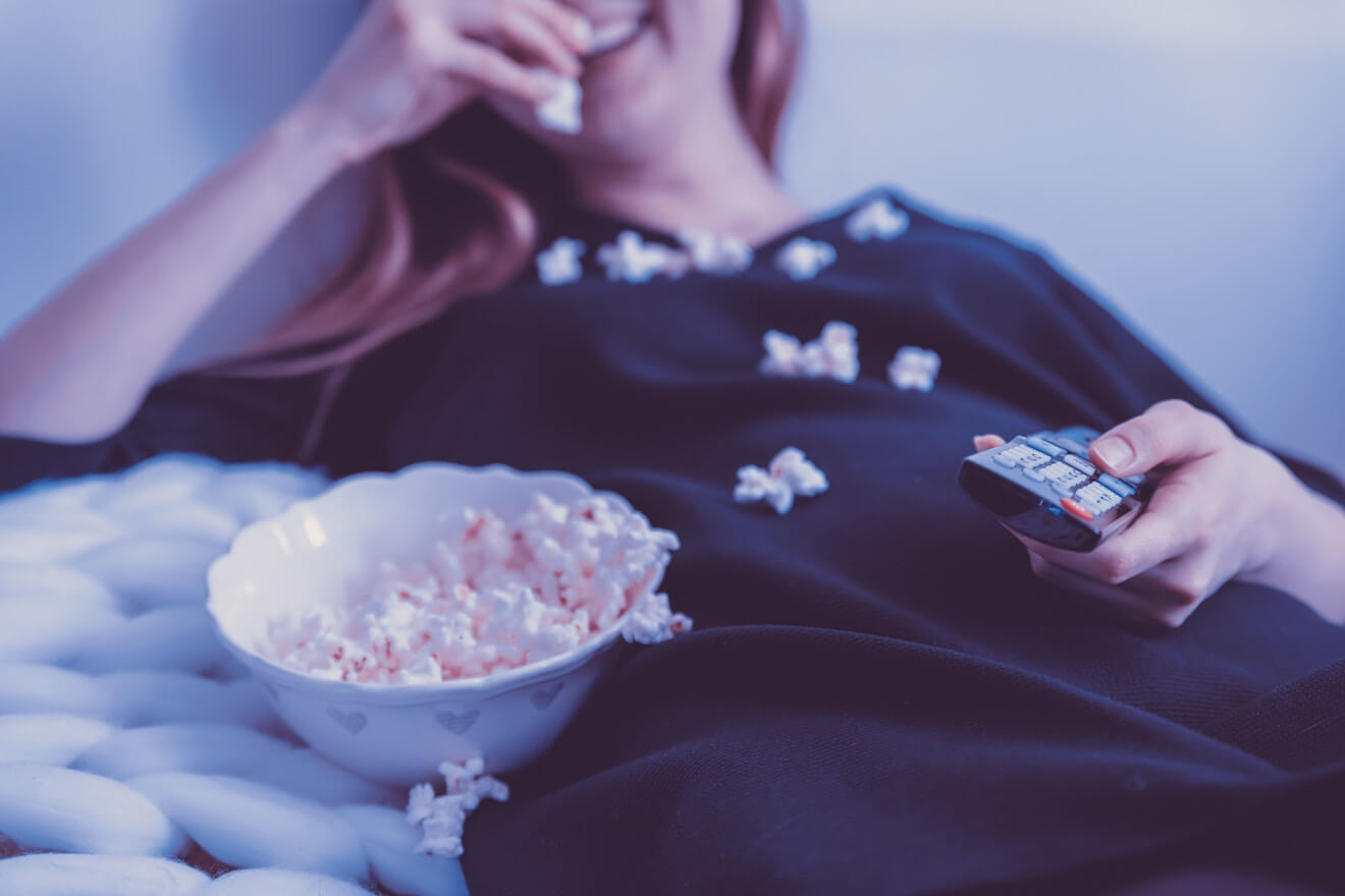 Woman watching tv on couch messily eating popcorn