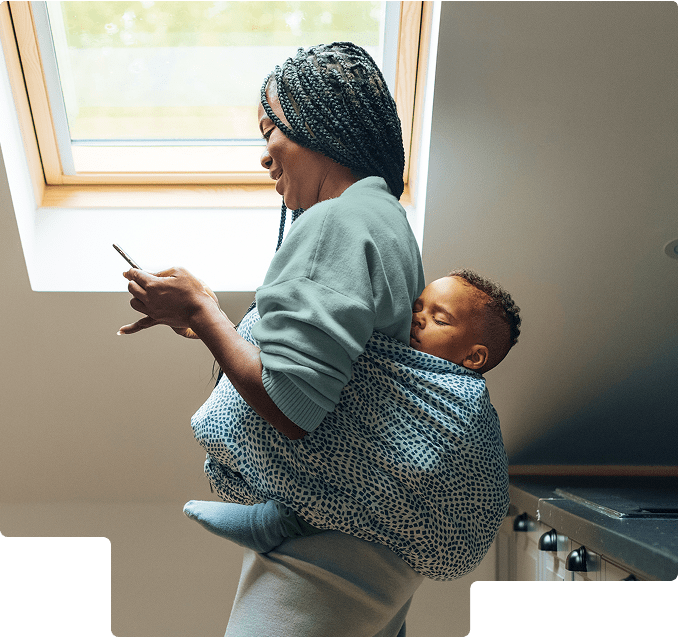 Woman looking at her phone with a child sleeping on her back